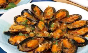 Un plato de mejillones a la marinera, jugosos y con una salsa sabrosa, adornados con perejil fresco.