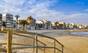 Escaleras de madera bajan a una playa vacía con edificios coloridos y palmeras al fondo. Un ejemplo de pueblos bonitos cerca de Benicàssim.