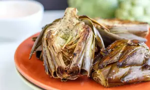 Deliciosas alcachofas al horno, doradas y tiernas, servidas en un plato naranja. Perfectas para disfrutar de su sabor.