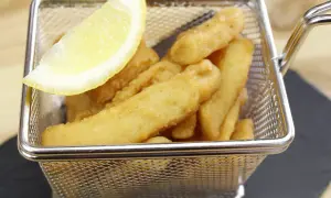 Deliciosos chocos fritos crujientes en una cesta metálica, acompañados de una rodaja de limón.