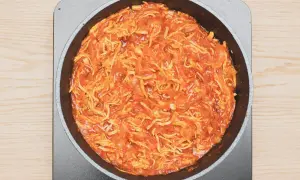 Tinga de pollo cocinándose en una sartén, con trozos de pollo deshebrado y salsa roja.