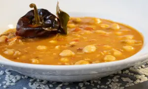 Un plato humeante de garbanzos con arroz, decorado con un pimiento seco y una hoja de laurel.