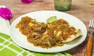 Un plato de urta a la roteña, con su jugoso pescado cubierto de cebolla y pimientos caramelizados, listo para disfrutar.