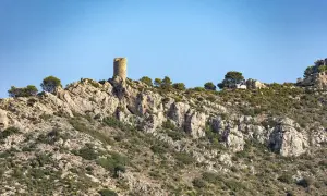 Torreón solitario en la cima rocosa del Desierto de las Palmas, vigilando un paisaje árido y escarpado bajo un cielo azul.