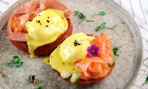 Dos deliciosos huevos benedictinos, uno con jamón y otro con salmón ahumado y aguacate, servidos sobre pan tostado con salsa holandesa.