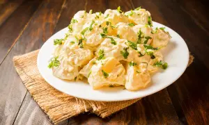 Patatas alioli cremosas y deliciosas, cubiertas con perejil fresco, servidas en un plato blanco sobre una mesa de madera rústica.