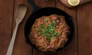 Un delicioso chili con carne humeante en sartén de hierro fundido, adornado con frijoles rojos y cilantro fresco.