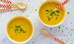 Dos cuencos de cremoso pure de verduras, decorados con perejil picado y cucharas de madera con lunares rojos.