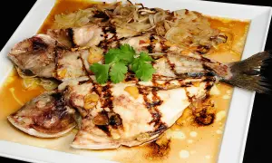 Dorada a la espalda, jugosa y a la parrilla, servida con cebolla caramelizada, ajo y cilantro fresco en una salsa dorada.
