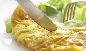 Un cuchillo corta una dorada tortilla francesa junto a hojas de lechuga fresca.