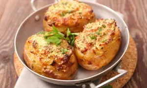 Tres patatas rellenas doradas y crujientes, cubiertas con queso rallado y perejil fresco, servidas en una sartén metálica.