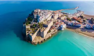 Castellón Costa Azahar: un pueblo amurallado con un castillo se alza sobre el mar turquesa, con un puerto deportivo y playas doradas.
