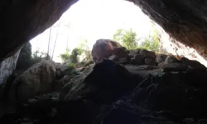 Salida de la cueva negra Montanejos, con rocas y vegetación iluminadas por el sol.