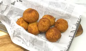 Croquetas de gambas doradas y crujientes, servidas en una bandeja con papel de periódico.