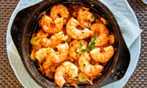 Deliciosos langostinos al ajillo burbujeando en aceite de oliva, con trozos de ajo y perejil fresco. ¡Un plato que huele a gloria!
