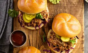 Dos jugosos sándwiches de pulled pork con pepinillos y col morada sobre pan rústico, listos para disfrutar.