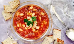 Un tazón de alubias con verduras, servido con pan rústico.