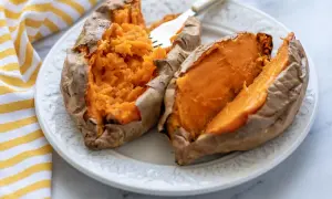 Dos mitades de boniato cocinado en freidora de aire, servidas en un plato blanco con un tenedor.