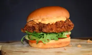 Deliciosa hamburguesa de pollo crujiente con lechuga, tomate y pepino, cubierta con una cremosa salsa.