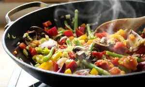 Un delicioso salteado de verduras humeante en un wok, con pimientos, judías verdes, champiñones y cebolla morada.