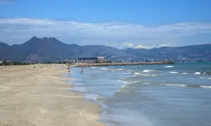 La playa del Serradal, con sus montañas al fondo, invita a pasear por la orilla mientras las olas acarician la arena dorada.