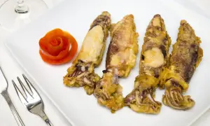 Cuatro chipirones fritos dorados y crujientes, servidos en un plato blanco con una rosa de tomate y cubiertos.