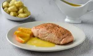 Filete de salmón a la naranja, servido con gajos de naranja y una salsa dorada. Acompaña unas patatas.