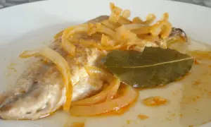 Deliciosa caballa en escabeche, con cebolla caramelizada y hoja de laurel, servida en un plato blanco.