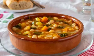Un plato de barro con una sabrosa comida típica de Castellón: judías blancas, patatas, zanahoria y verduras en un caldo reconfortante.