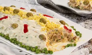 Ensaladilla rusa, receta de la abuela, cubierta de mayonesa, aceitunas, huevo rallado y pimientos.