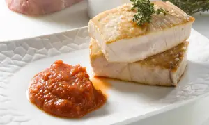 Dos trozos de atún a la plancha apilados, con una guarnición de salsa de tomate y una ramita de tomillo.