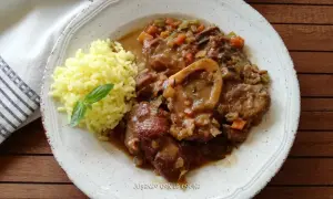 Un plato de osso buco con arroz amarillo y una hoja de albahaca. La carne está cubierta de una salsa con verduras.