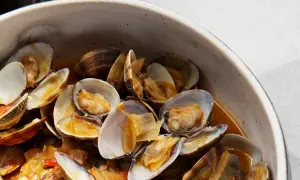 Un tazón lleno de almejas a la marinera, con sus conchas abiertas y jugosas, nadando en una salsa dorada.