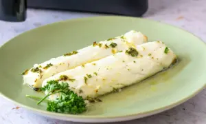 Dos filetes de merluza jugosa, recién hechos en airfryer, con hierbas frescas y aceite de oliva.
