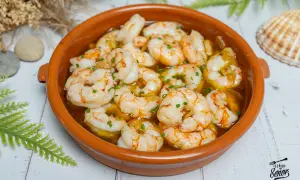Un plato de gambas al ajillo burbujeantes en una cazuela de barro, adornado con perejil picado.