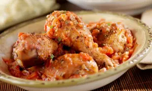 Sabroso pollo guisado en una salsa de tomate con hierbas, servido en un cuenco rústico.