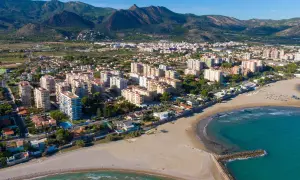 Vista aérea del casco antiguo de Benicàssim pueblo, con edificios residenciales, playas de arena y el mar Mediterráneo. Montañas verdes al fondo.