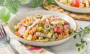 Un plato de ensalada de pasta tricolor con jamón, huevo duro, aceitunas y guisantes.