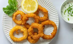 Crujientes aros de cebolla dorados, servidos con una rodaja de limón y un dip cremoso. ¡Un aperitivo irresistible!