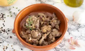 Mollejas de pollo guisadas con ajo y tomillo en cazuela de barro, acompañadas de granos de pimienta y una cabeza de ajo.