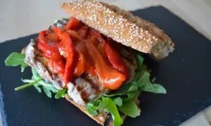 Un delicioso pepito de ternera con pimientos rojos asados y rúcula, servido en pan rústico con semillas.