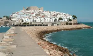 Pueblos costa Azahar: un castillo y casas blancas se alzan sobre una colina, con el mar turquesa y un rompeolas de rocas.