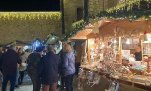 Gente pasea por el mercado navideño Peñíscola, con puestos de adornos y luces festivas.