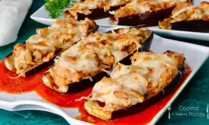 Berenjenas rellenas de atún gratinadas con queso, servidas sobre una base de salsa roja.