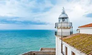El faro de Peñíscola se alza vigilante sobre el mar turquesa, con un cielo nublado que promete aventura.