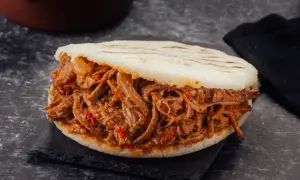 Arepa rellena de carne mechada jugosa y tierna, con trozos de pimiento rojo.