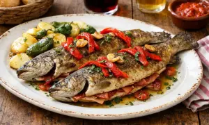 Trucha a la navarra, dos truchas enteras rellenas de jamón, acompañadas de patatas y pimientos, decoradas con pimientos rojos y perejil.