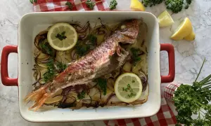 Deliciosos salmonetes al horno con patatas, cebolla roja, limón y perejil fresco, listos para servir.