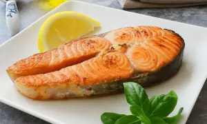 Un jugoso salmón a la plancha, servido con una rodaja de limón y hojas de albahaca fresca en un plato blanco.