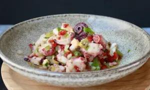 Salpicon de pulpo fresco con pimientos, cebolla y perejil, servido en un cuenco rústico.